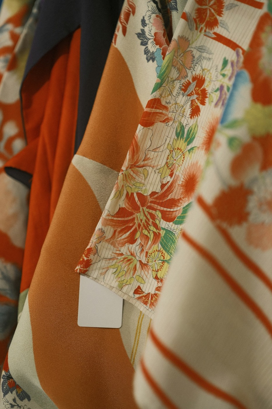 Kimonos anciens en soie suspendus, motifs floraux vermillon et ivoire.