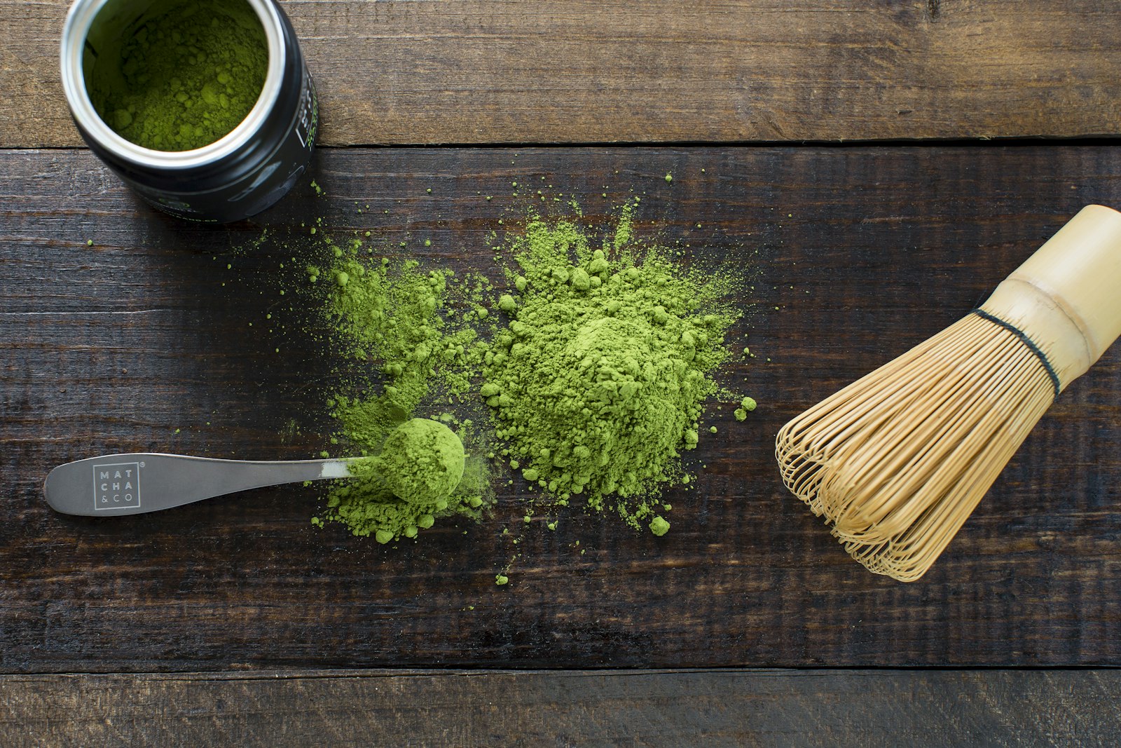 Matcha en poudre et fouet en bambou sur un plateau de bois sombre.