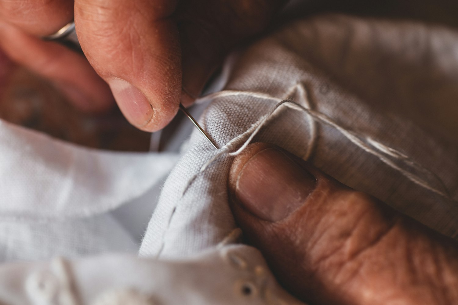 Gros plan de mains cousant à la main un tissu clair.